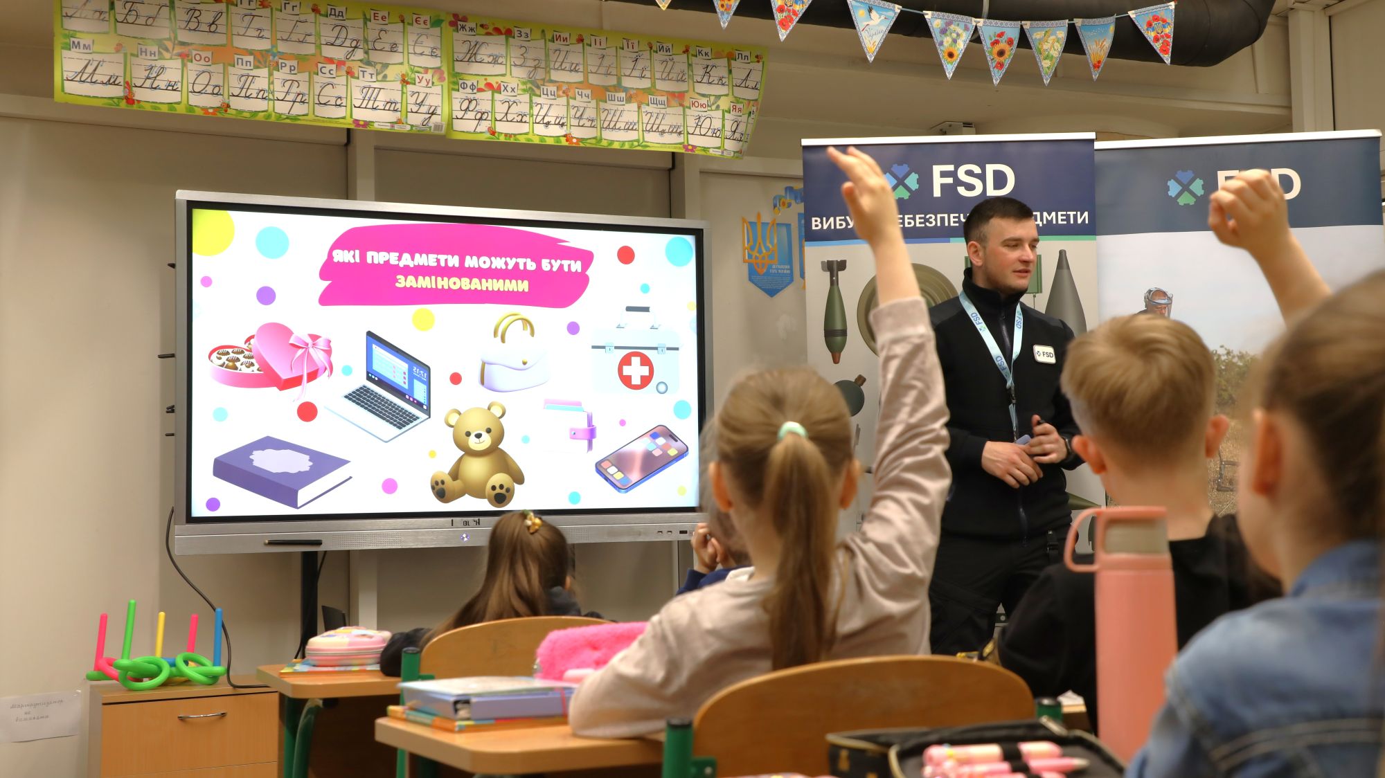 FSD-Trainer erklärt Kindern in einem Klassenzimmer in Charkiw, welche Alltagsgegenstände vermint sein können
