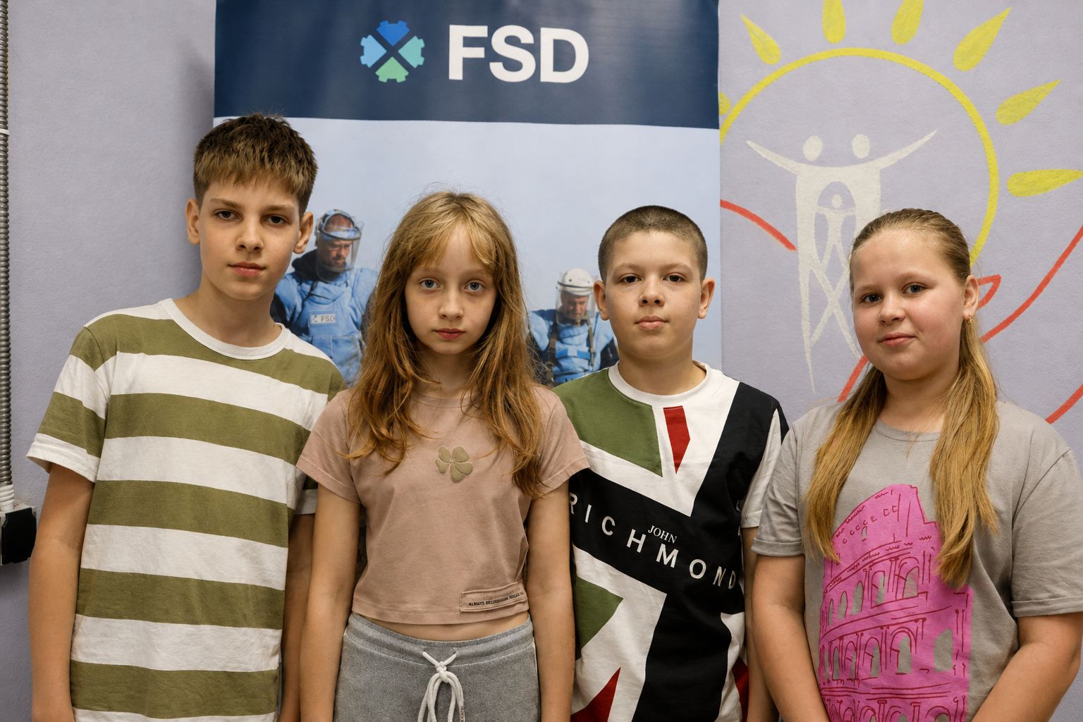 Vier Kinder aus Charkiw stehen vor einem FSD-Banner nach einer Risikoaufklärung zu Landminen