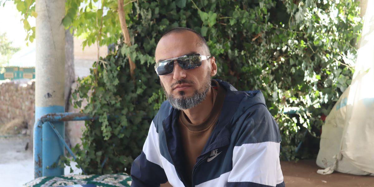 Khusrav Rafiev sitzt mit Sonnenbrille vor einer begrünten Wand im Freien.