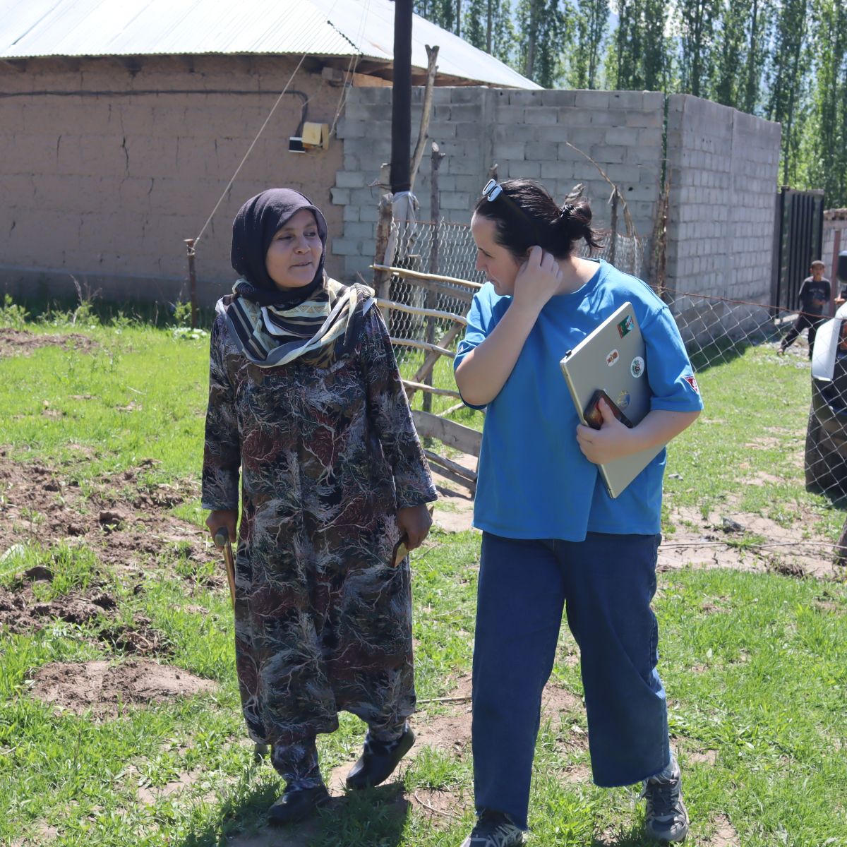 Eine Frau mit Gehhilfe und eine FSD-Mitarbeiterin gehen durch einen Garten in Tadschikistan.