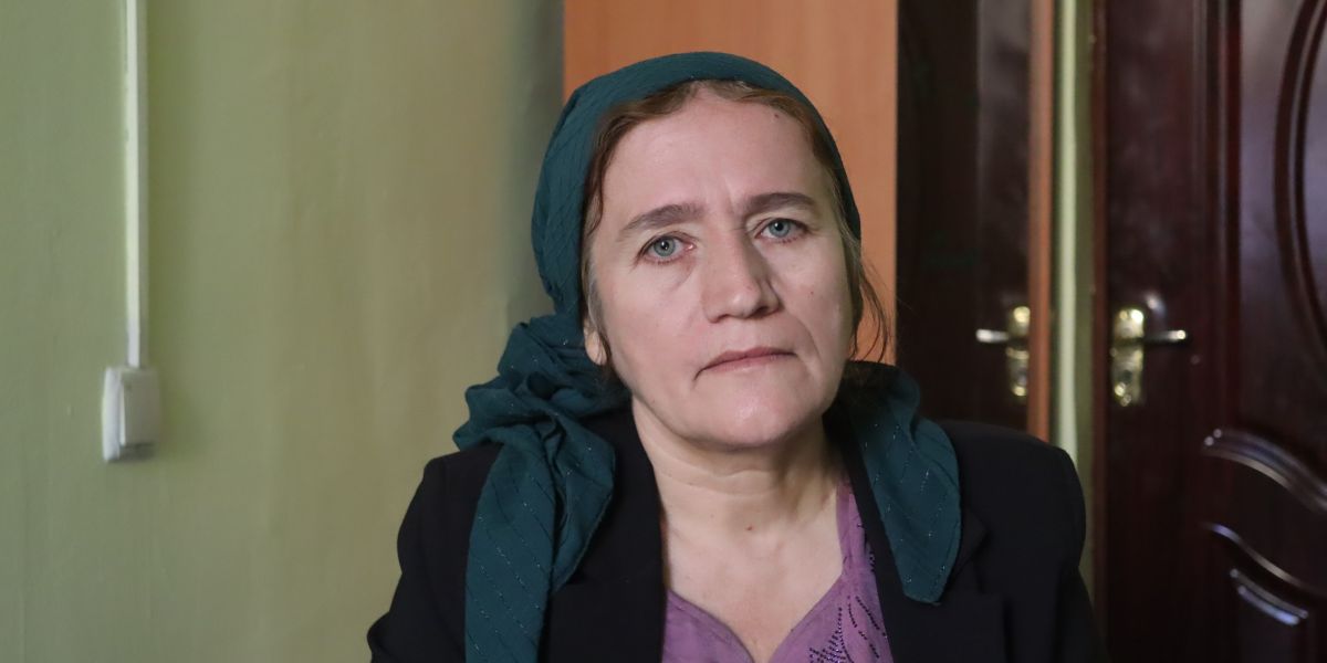 Zebuniso Nazrieva mit petrolfarbenem Kopftuch vor einer Tür.