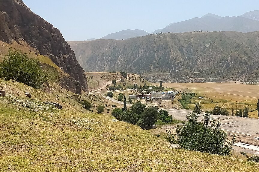 Berglandschaft in Tadschikistan mit steilen Felshängen, einer Straße und einzelnen Gebäuden im Tal.